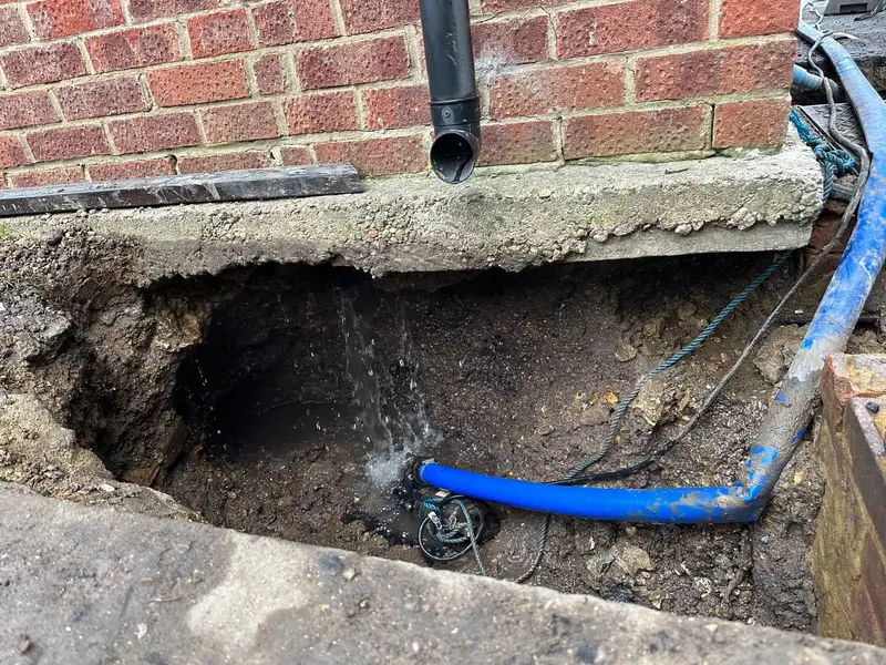 Blue water supply pipe in an excavation beside the brick wall of a property