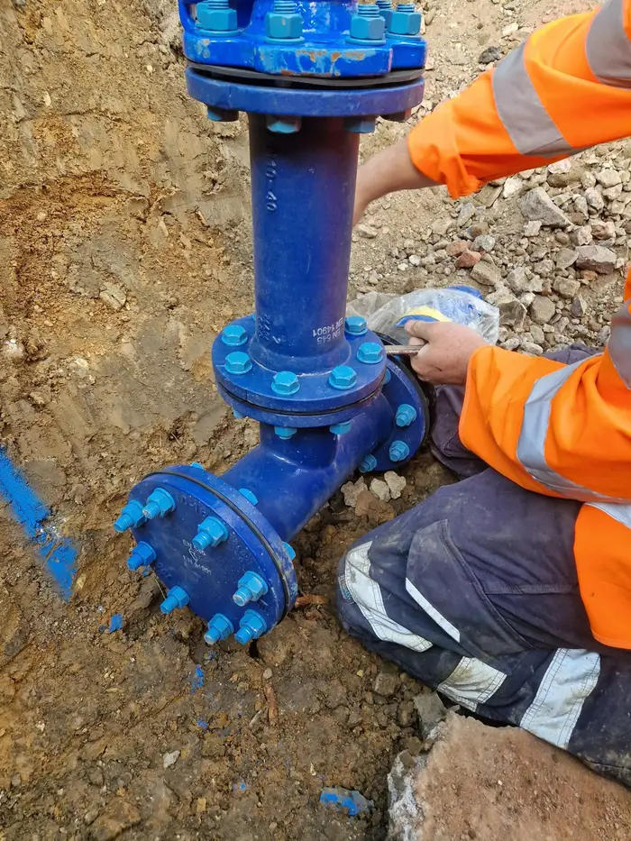 Engineer in hi-vis clothing fitting blue flanged water main pipework in an excavation