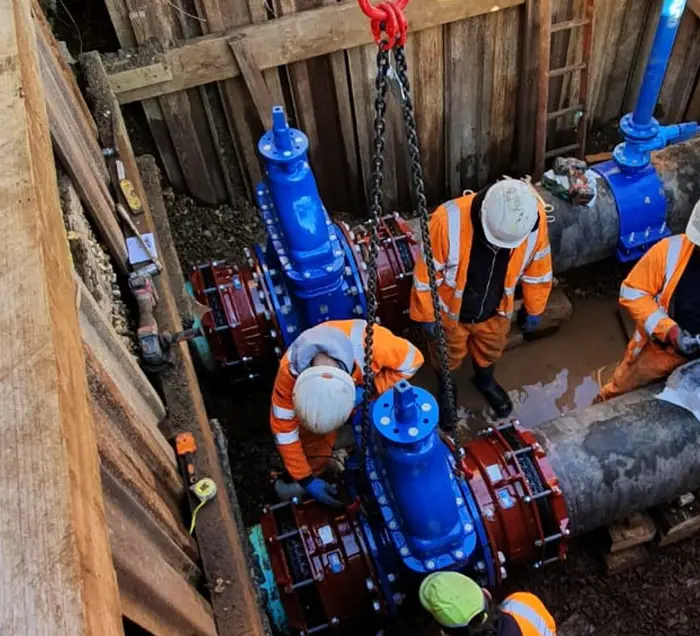 Engineers installing blue gate valves on a large-diameter water main in a timber-shored trench