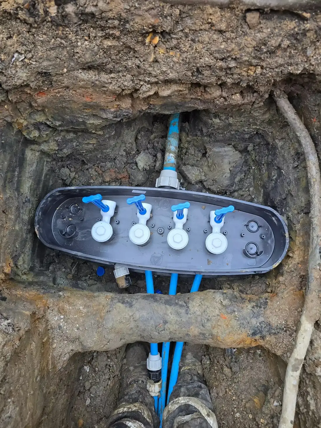 Four-port water meter manifold connected to blue supply pipes in an excavation